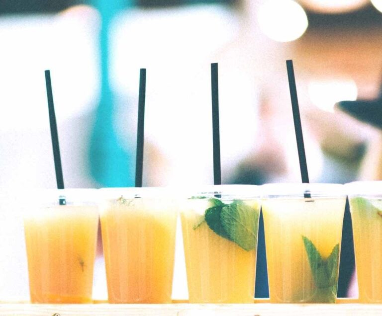 Four glasses of orange-colored drinks with black straws and mint leaves