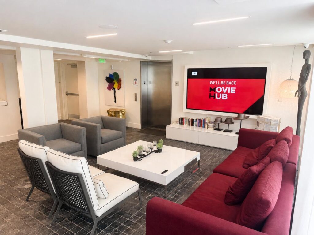 A seating area with a red couch, gray chairs, and a white coffee table in front of a large TV.