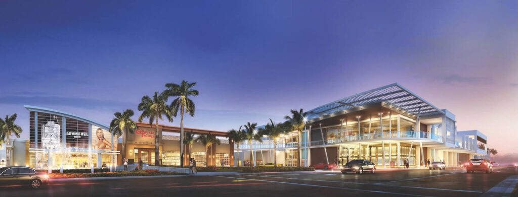 A modern building with palm trees and evening lights, with cars driving by on the road.