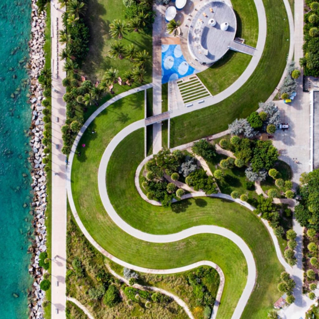 An aerial view of a winding path through a landscaped area with pools and a body of water.