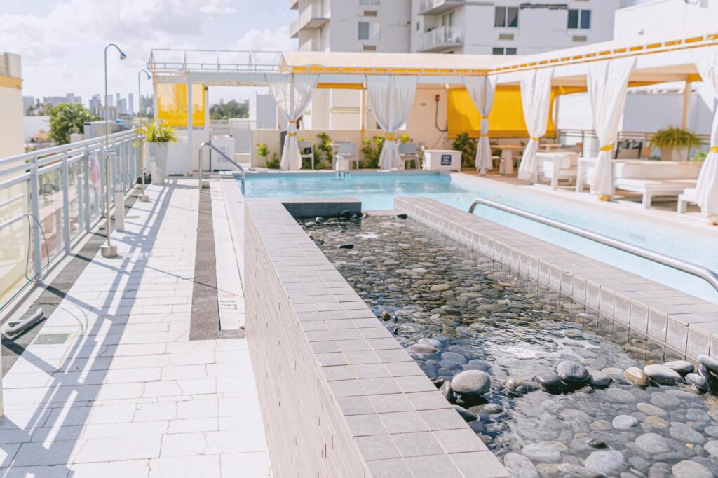 A rooftop pool with a water feature, seating area, and cabanas